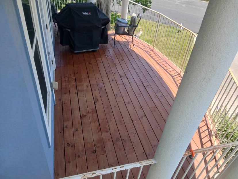Refinished deck boards on a covered porch beside a grill and seating